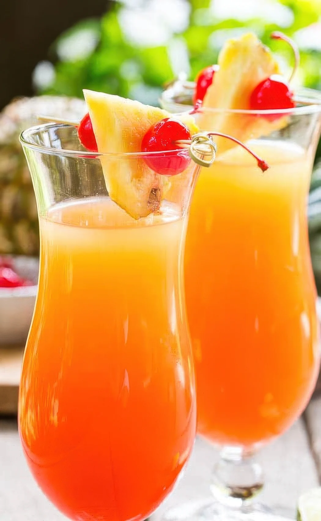 Two cocktails garnished with cherries and pineapple.