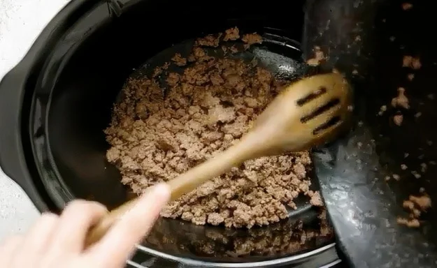 Ground beef being transferred to slow cooker.