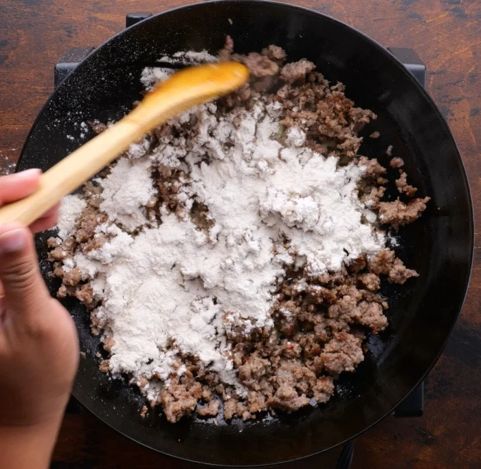Sprinkling flour over sausage.