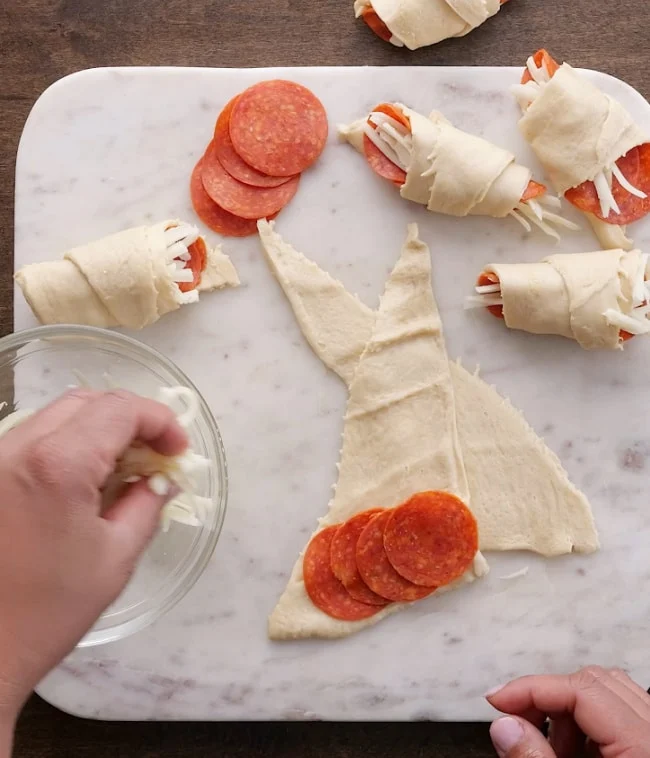 Placing pepperoni and cheese on crescent dough.