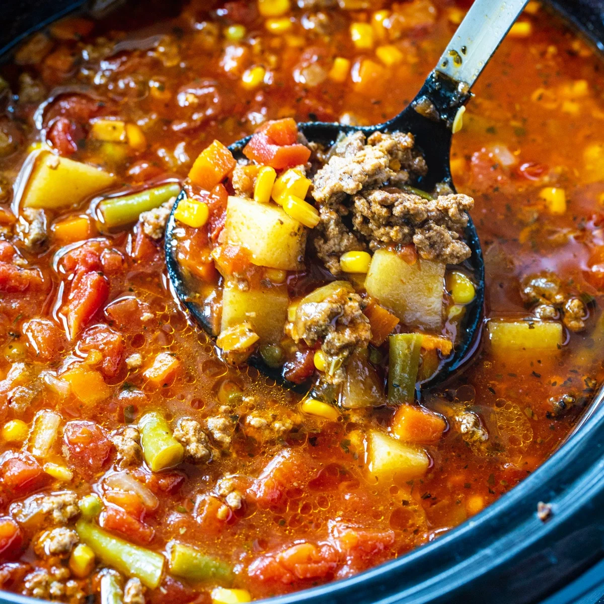 Spoon scooping up vegetable soup out of slow cooker.
