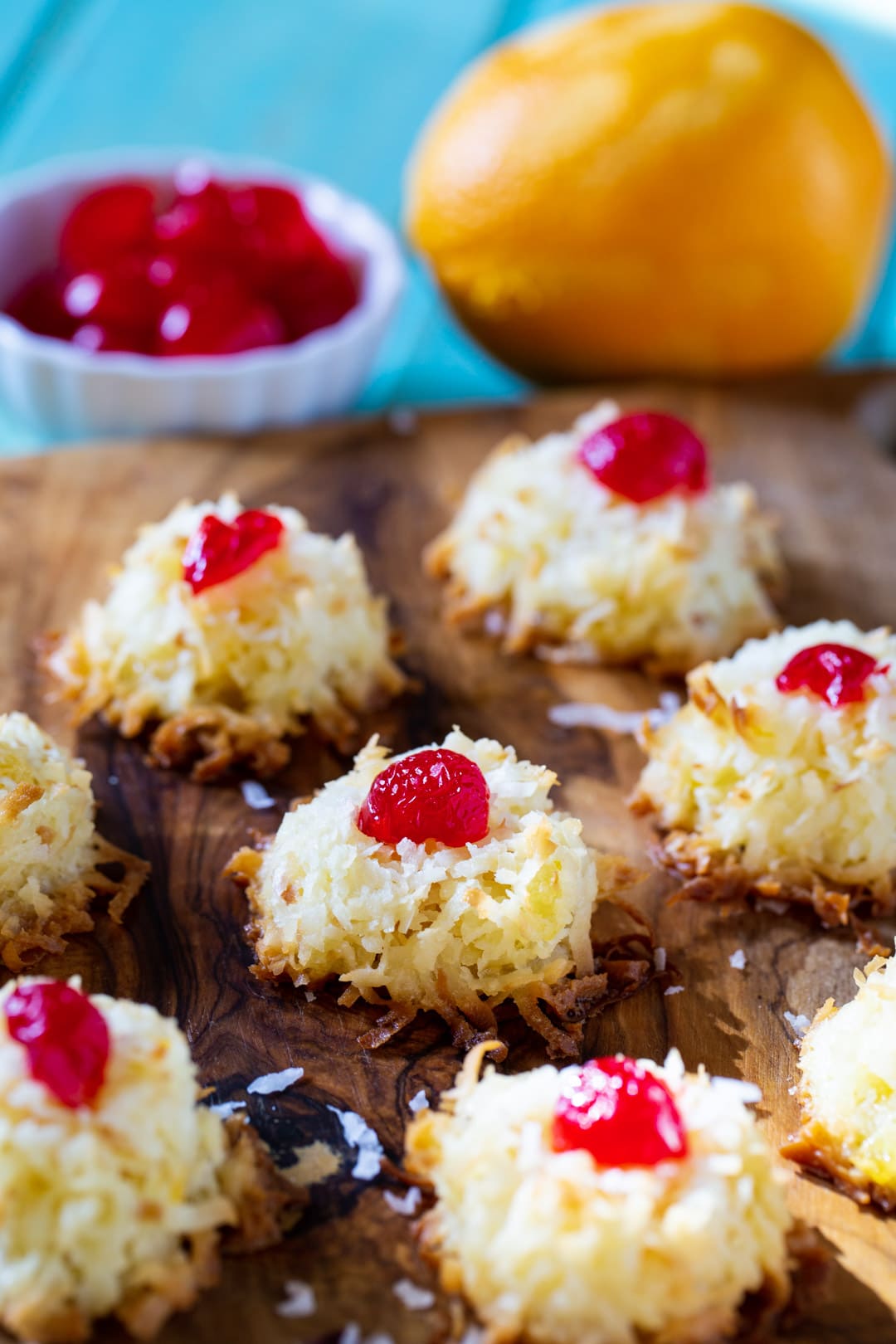 Ambrosia Macaroons on a wood board and a bowl of cherries.