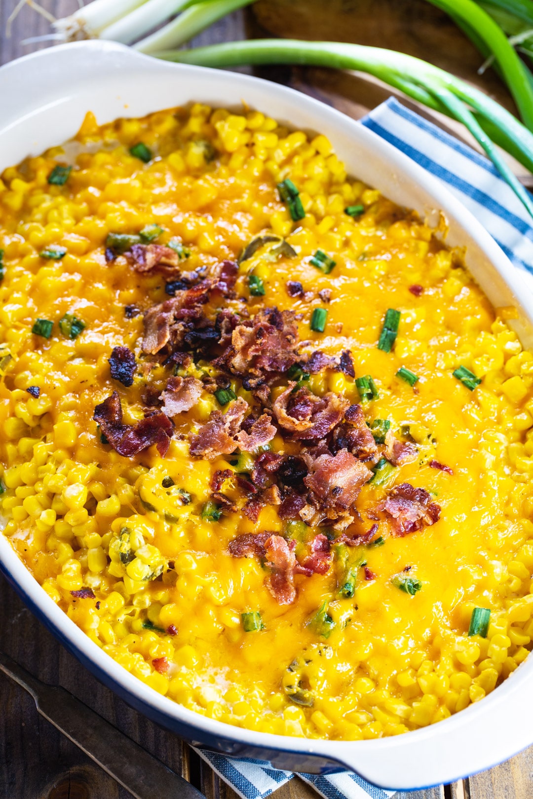 Cooked corn casserole topped with crumbled bacon in casserole dish.
