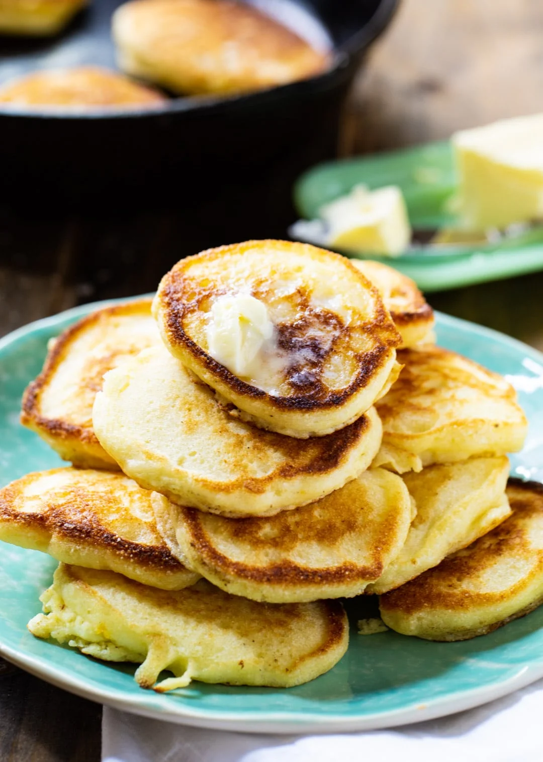 Hoe Cakes on a plate with cast iron pan in background.