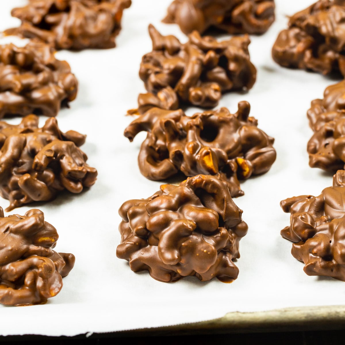 Chocolate Peanut Clusters with Pretzels on parchment paper.