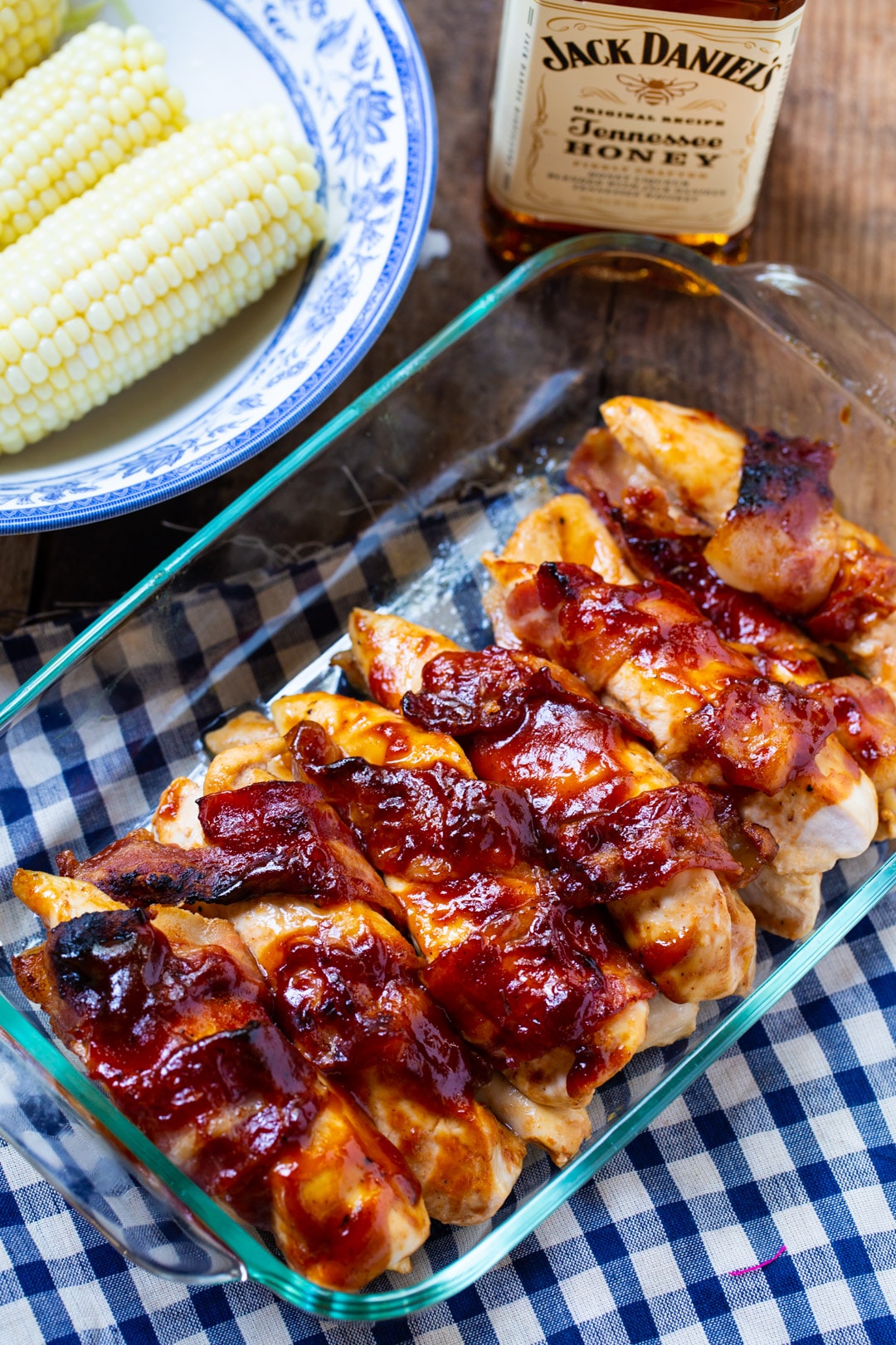 Cooked BBQ Chicken in a 9x13-inch baking dish, bowl of corn, and bottle of bourbon.