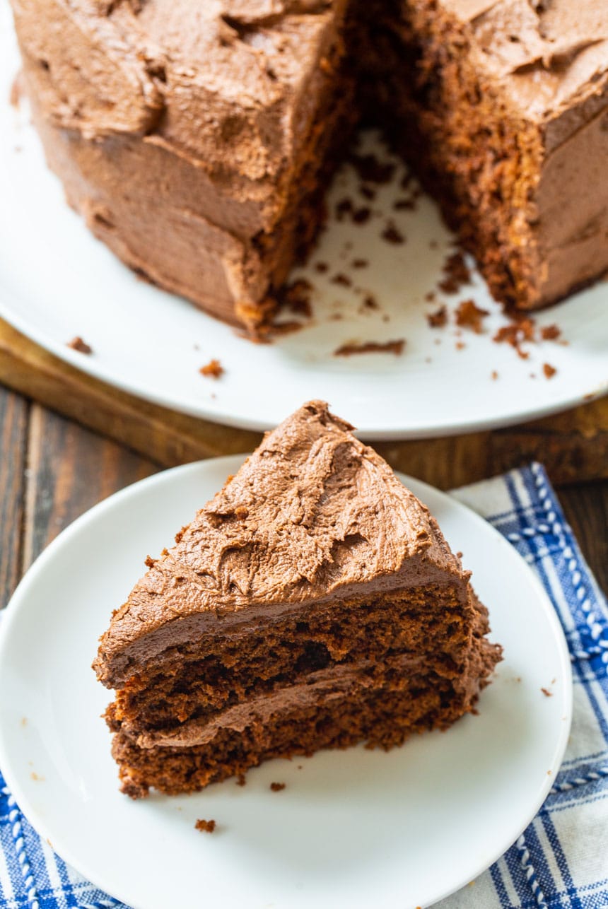 Slice of Chocolate Layer Cake on plate with rest of cake in background.