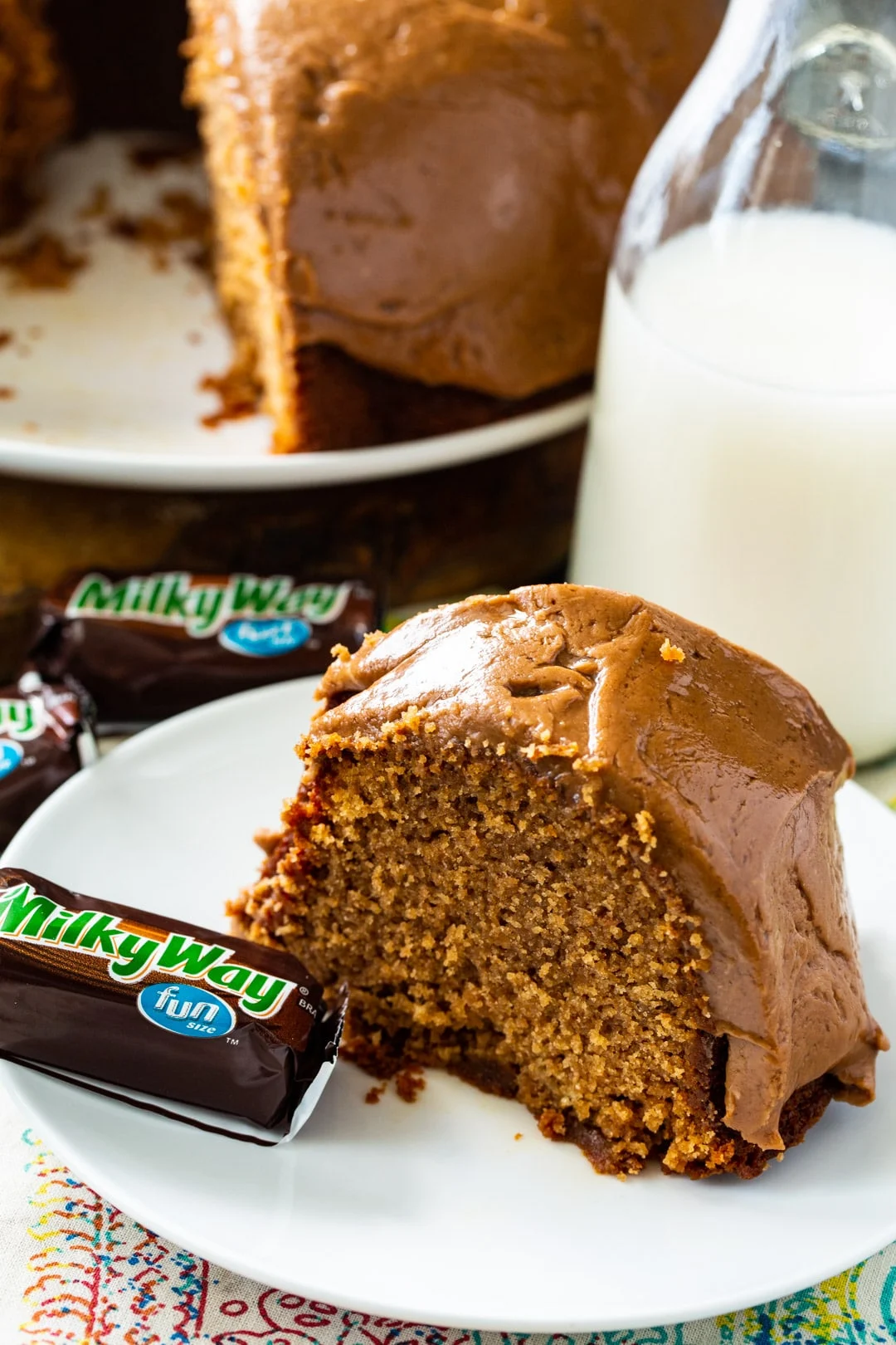 Slice of cake and candy bar on plate with rest of cake in background.