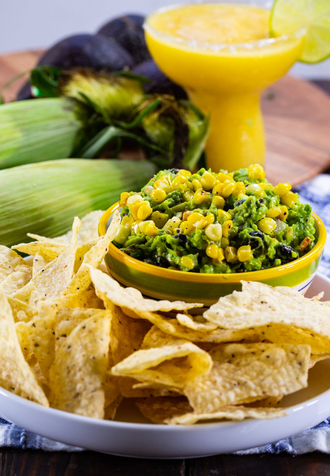 Guacamole and chips on a plate with margarita in background.