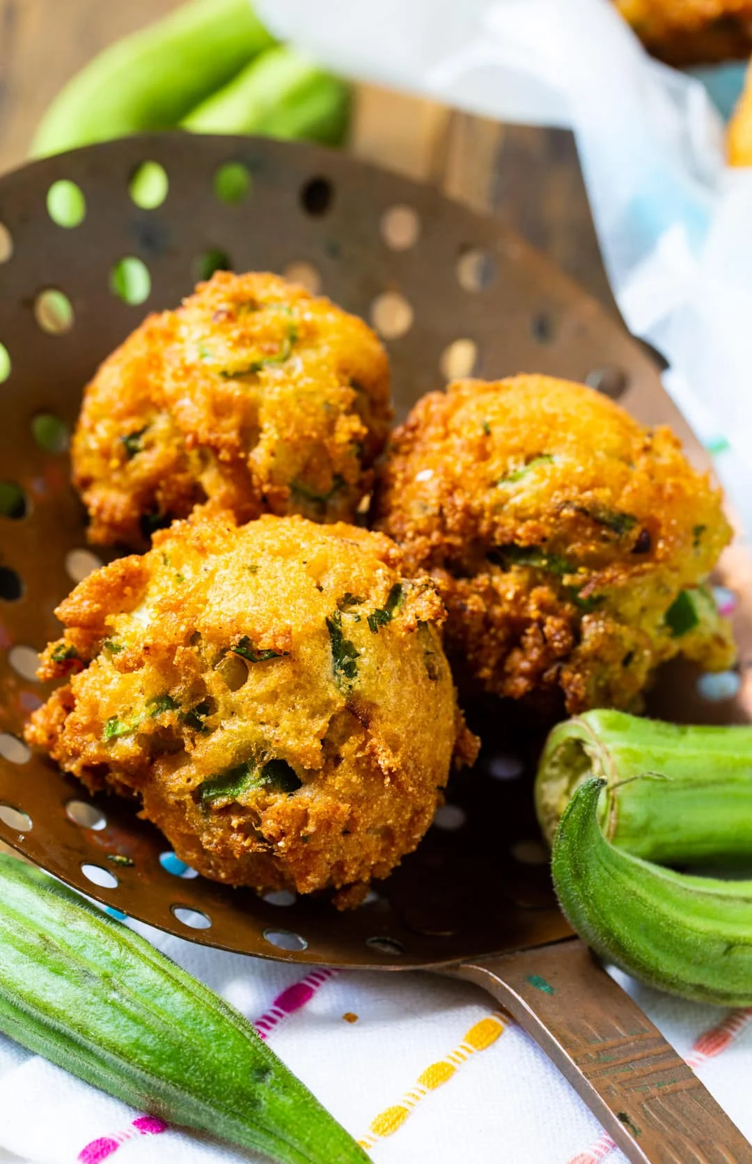 Three hush puppies on a metal strainer spoon.