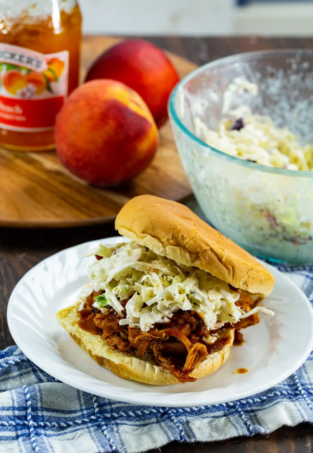 Pulled Chicken Sandwich on a p-late with peaches in background.