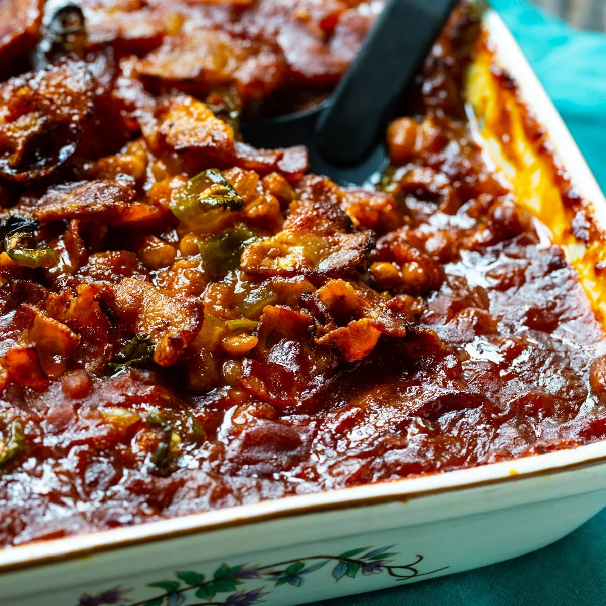 Spicy Bacon Baked Beans getting scooped out of baking dish.