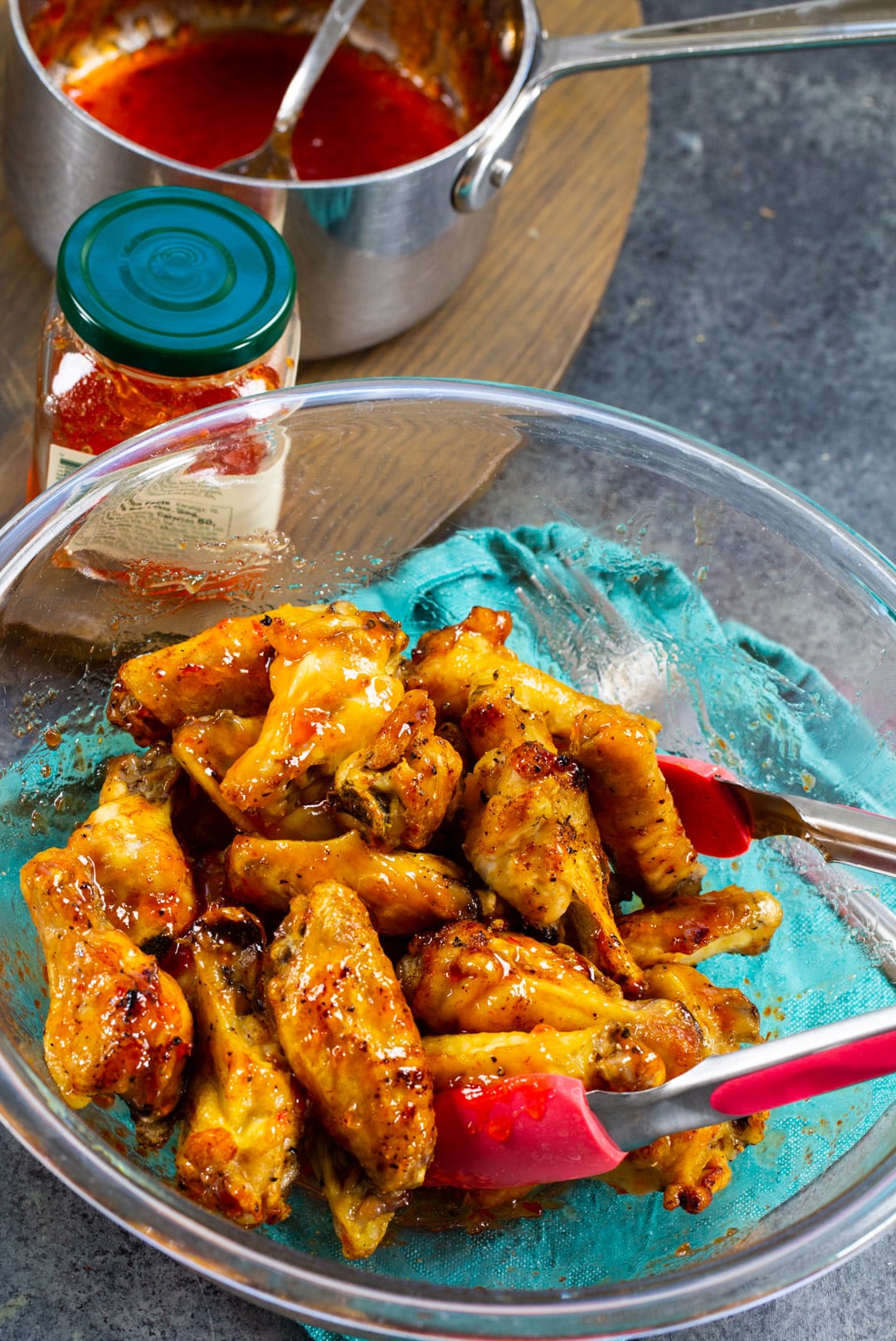 Wings being tossed with papper jelly glaze in a bowl.