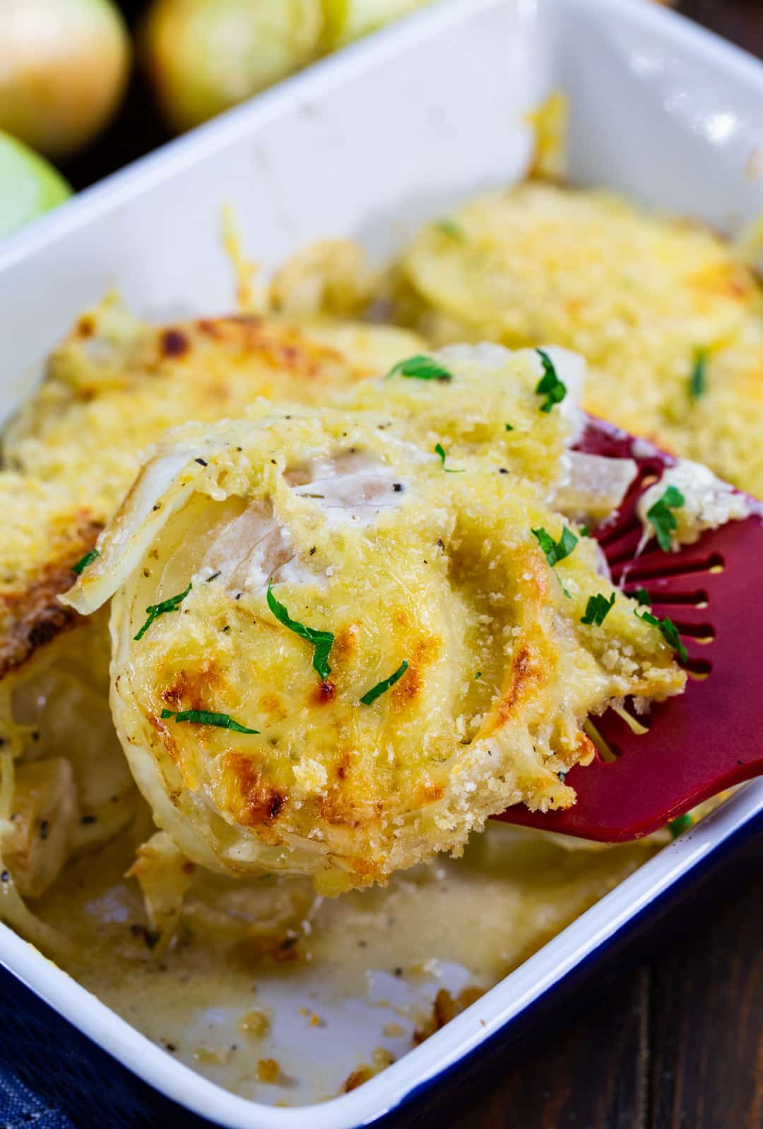 Spatula lifting Vidalia onions out of baking dish.