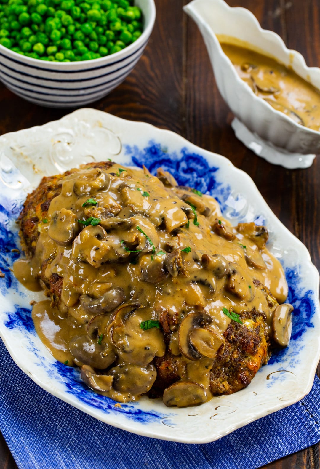 Meatloaf on a platter, gravy boat full of gravy and bowl of peas.