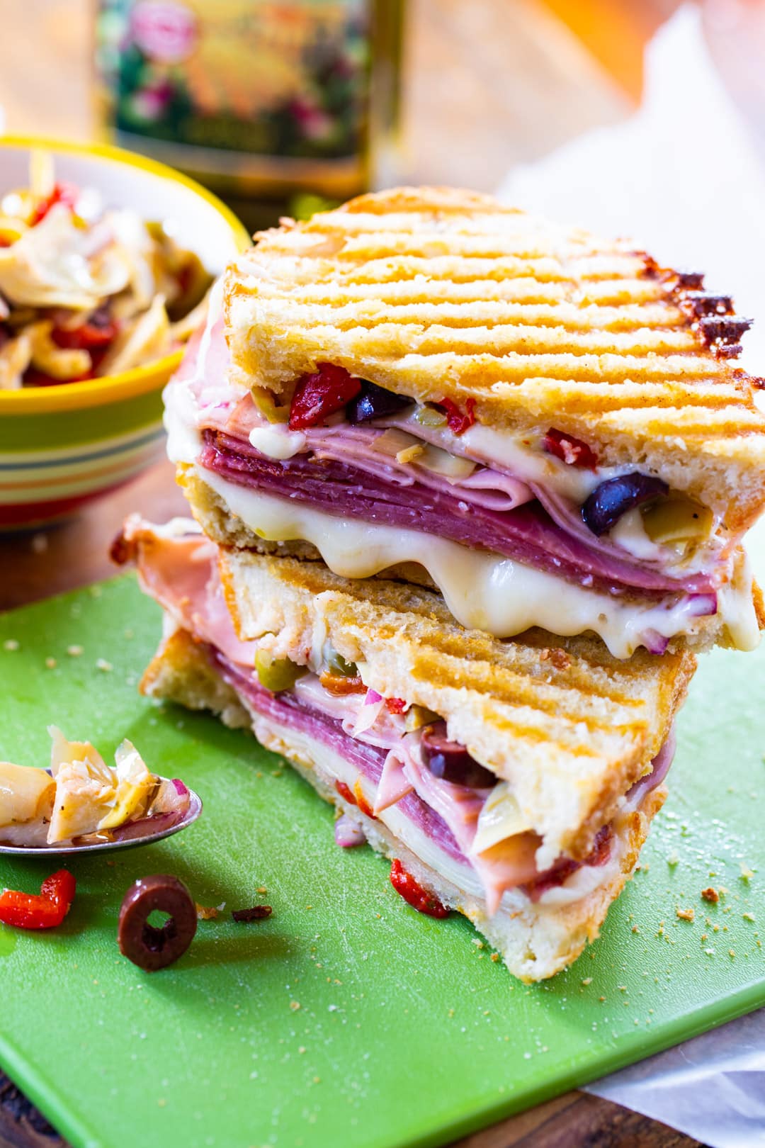 Panini on cutting board with bowl of olive salad.