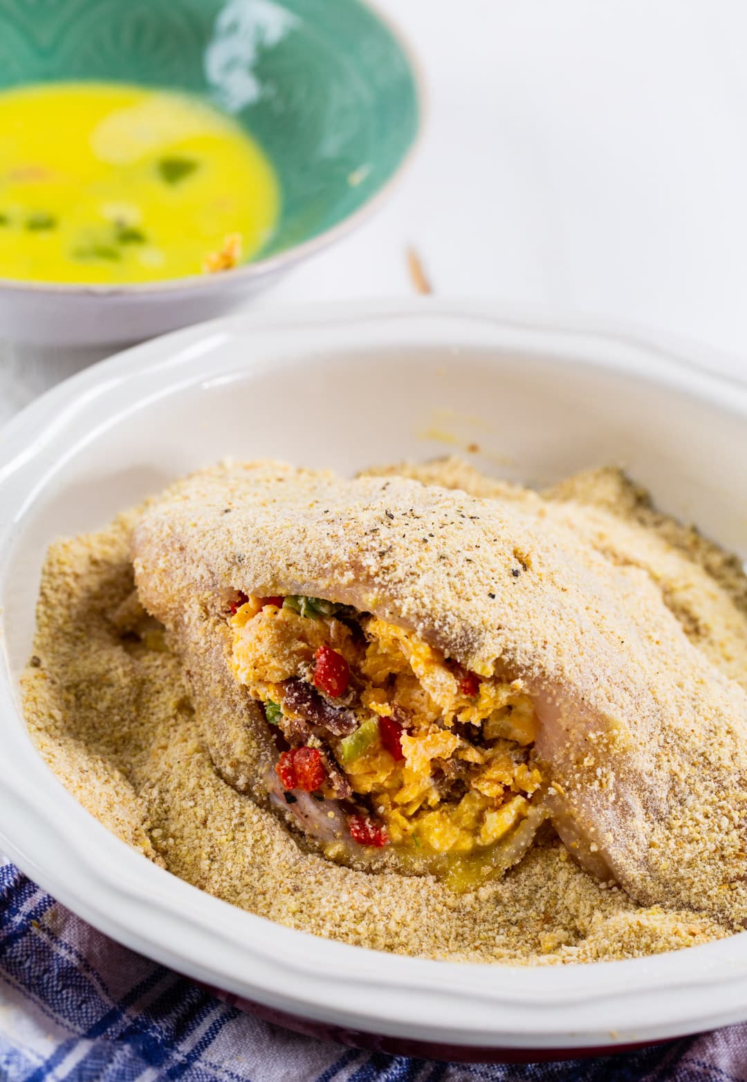 Chicken breast getting coated in bread crumbs.