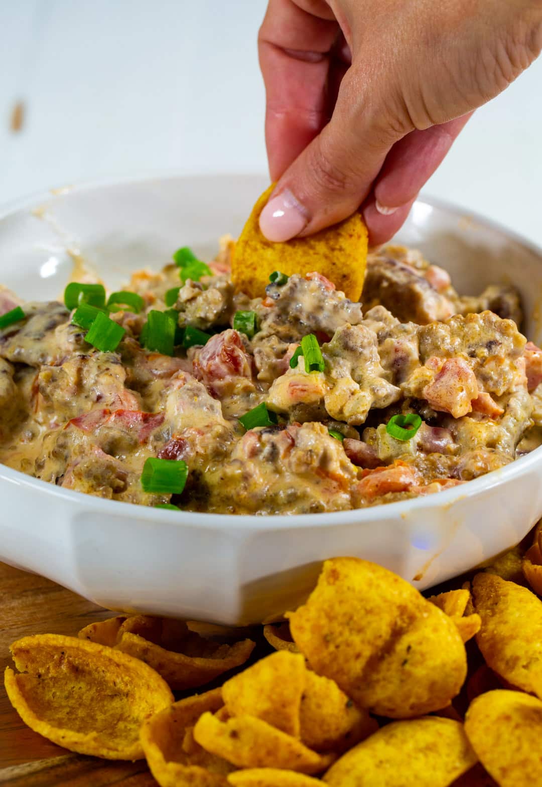 Hand sticking frito chip into dip.
