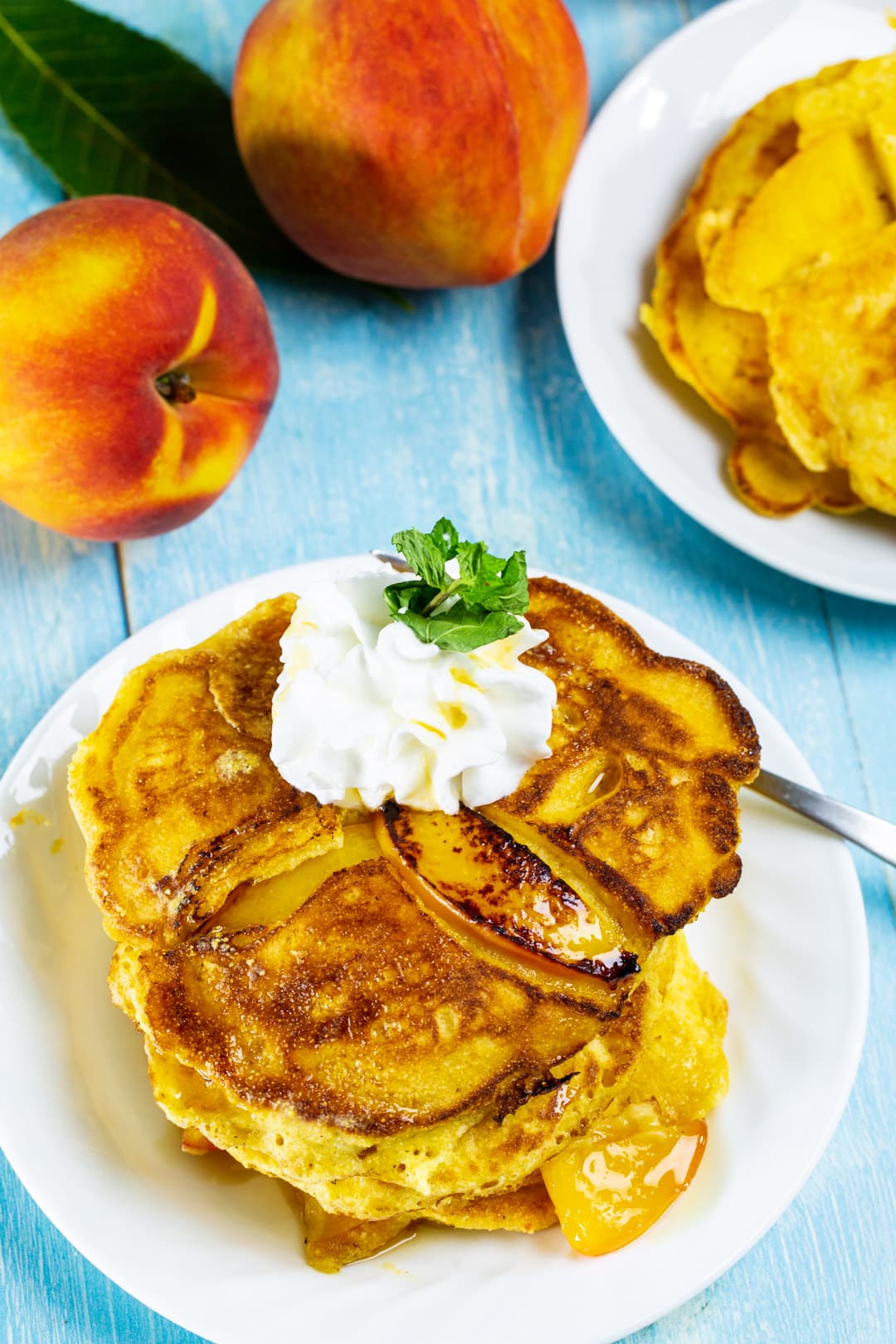 Pancakes stacked on a plate surrounded by fresh peaches.