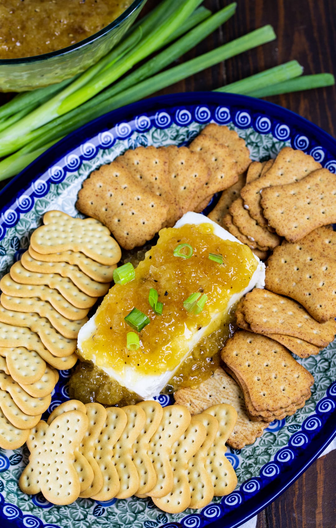 Cream cheese topped with sauce on a platter with crackers.