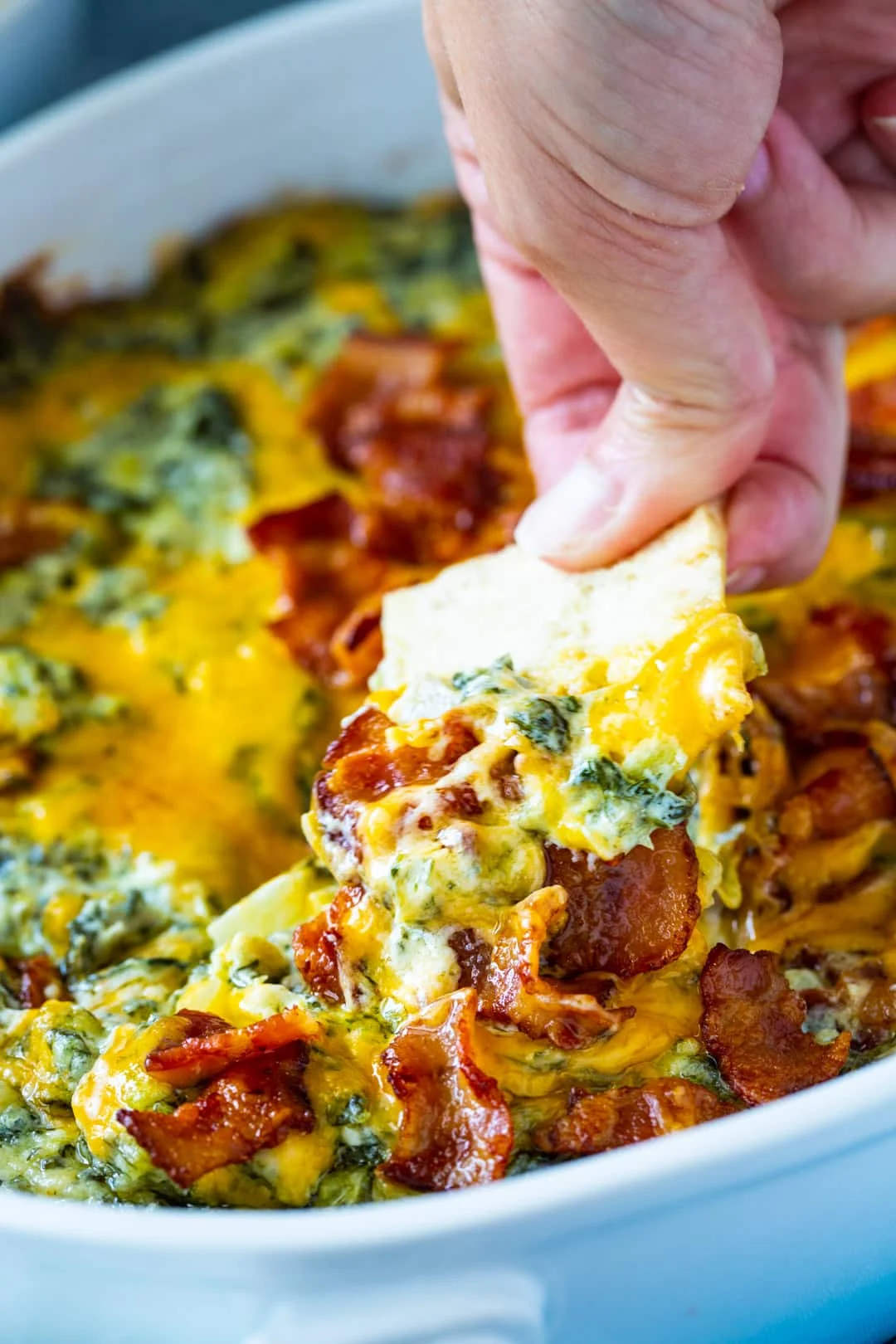 Hand scooping up dip with pita chip.