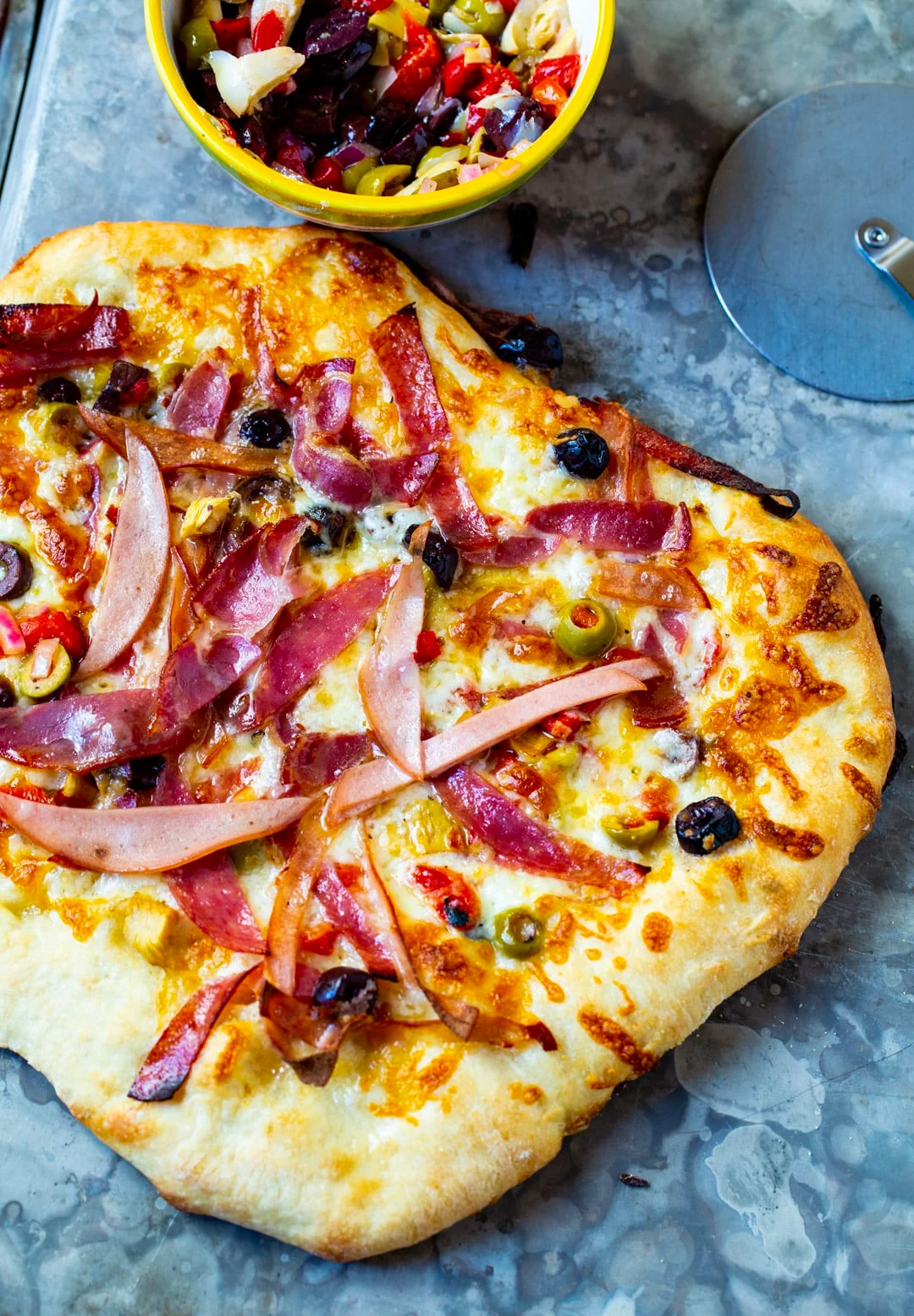 Whole pizza and a bowl of olive salad.