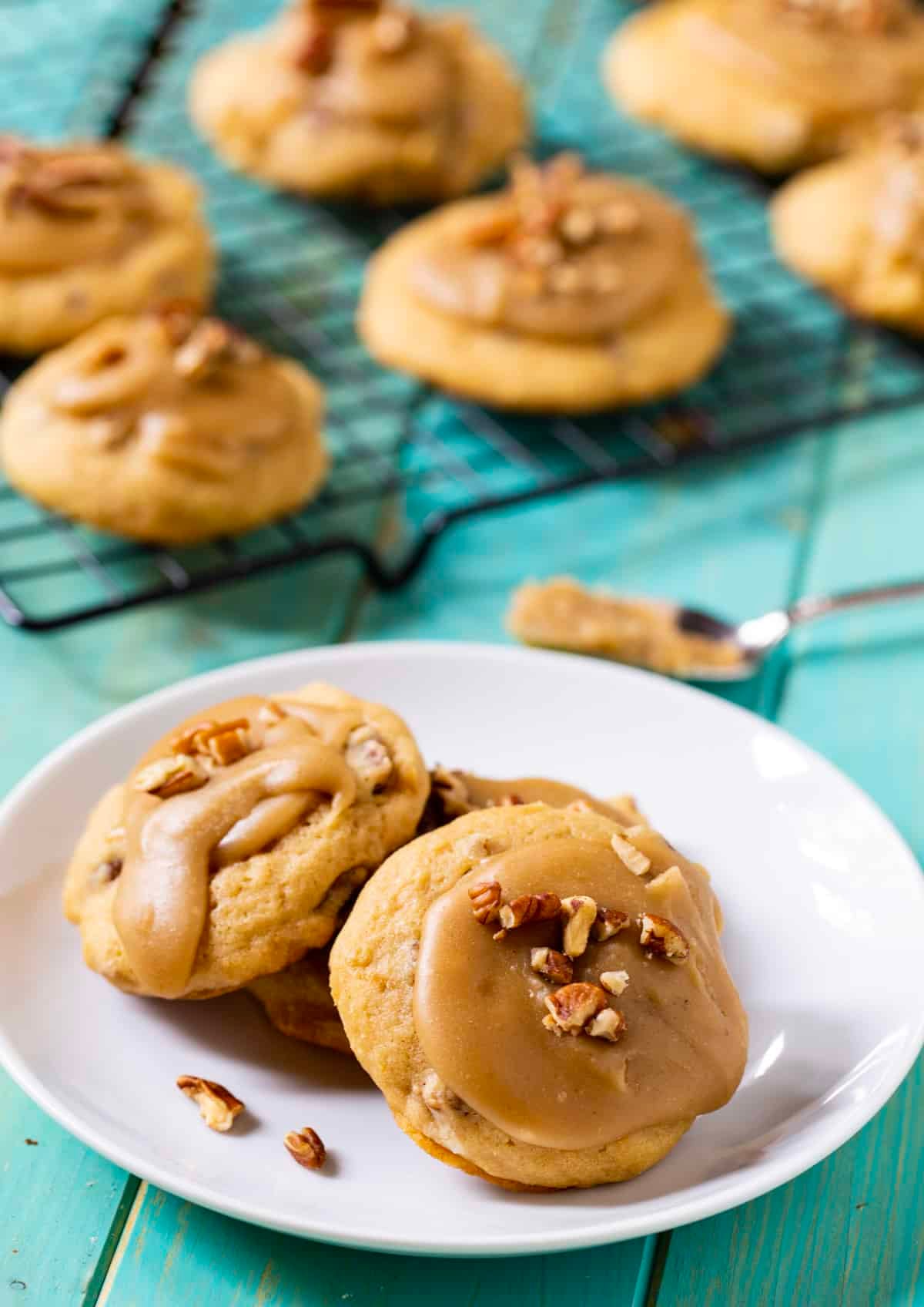 Caramel Frosted Brown Suagr Cookies on a plate and a wire rack.