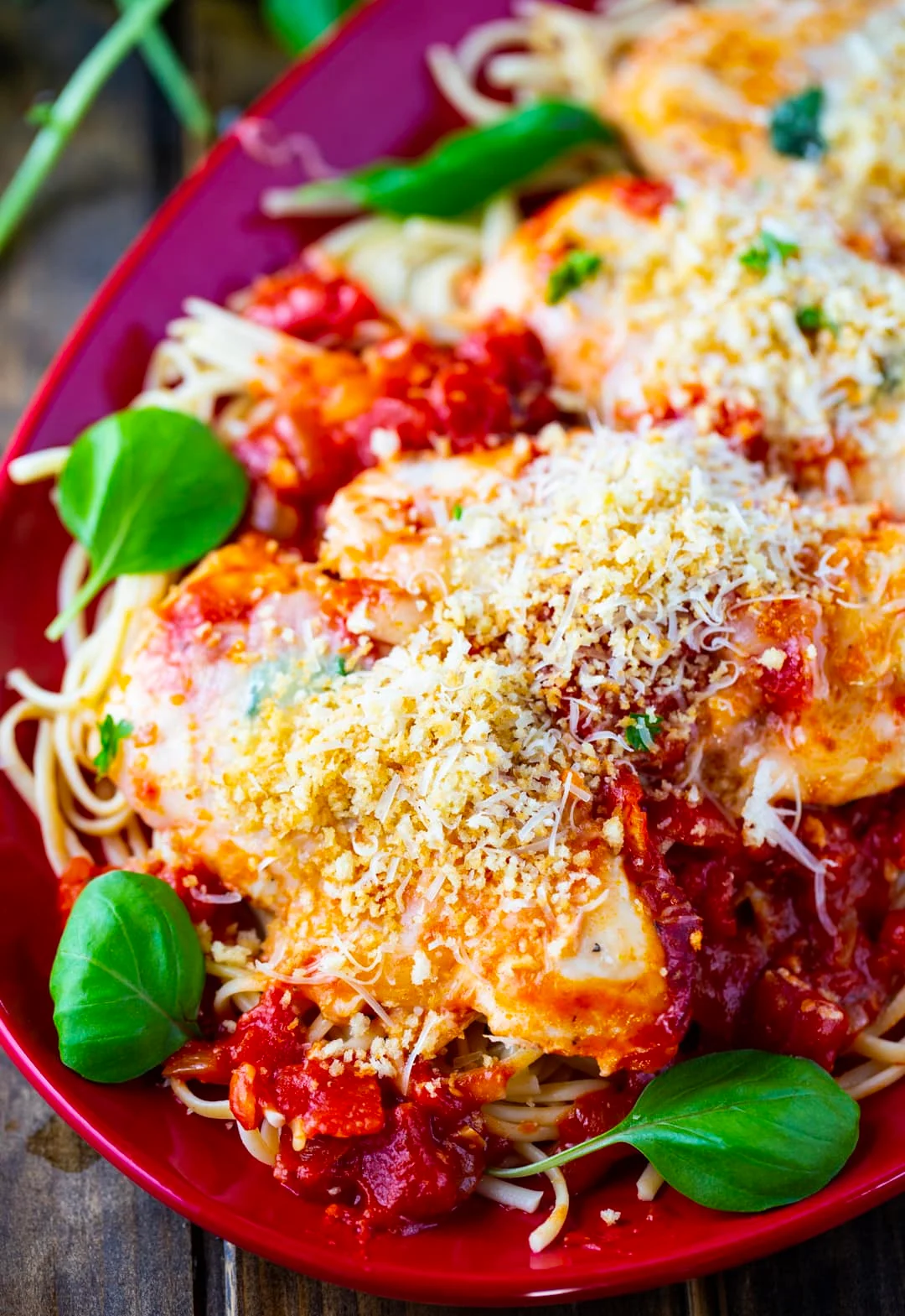 Chicken over pasta on a plate with fresh basil.
