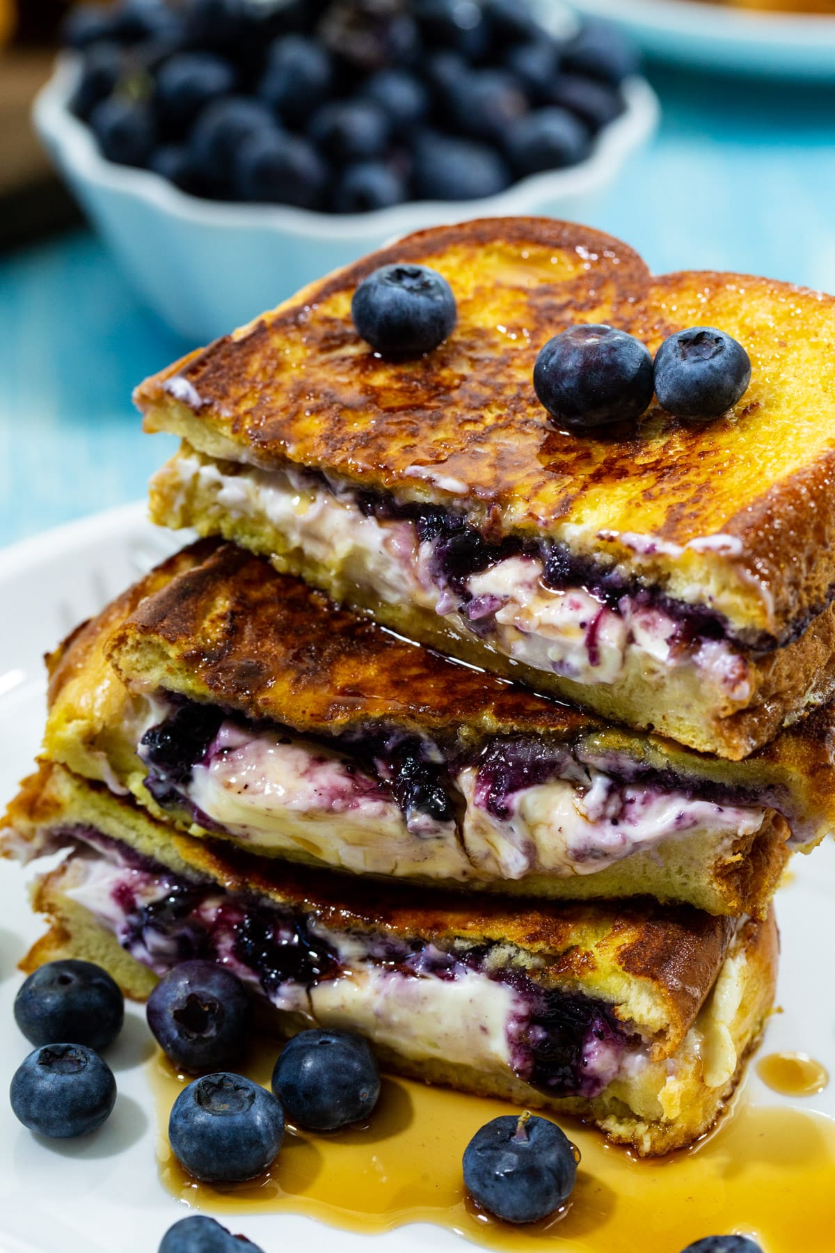 Blueberry Stuffed French Toast halves stacked up on a plate and drizzled with maple syrup.