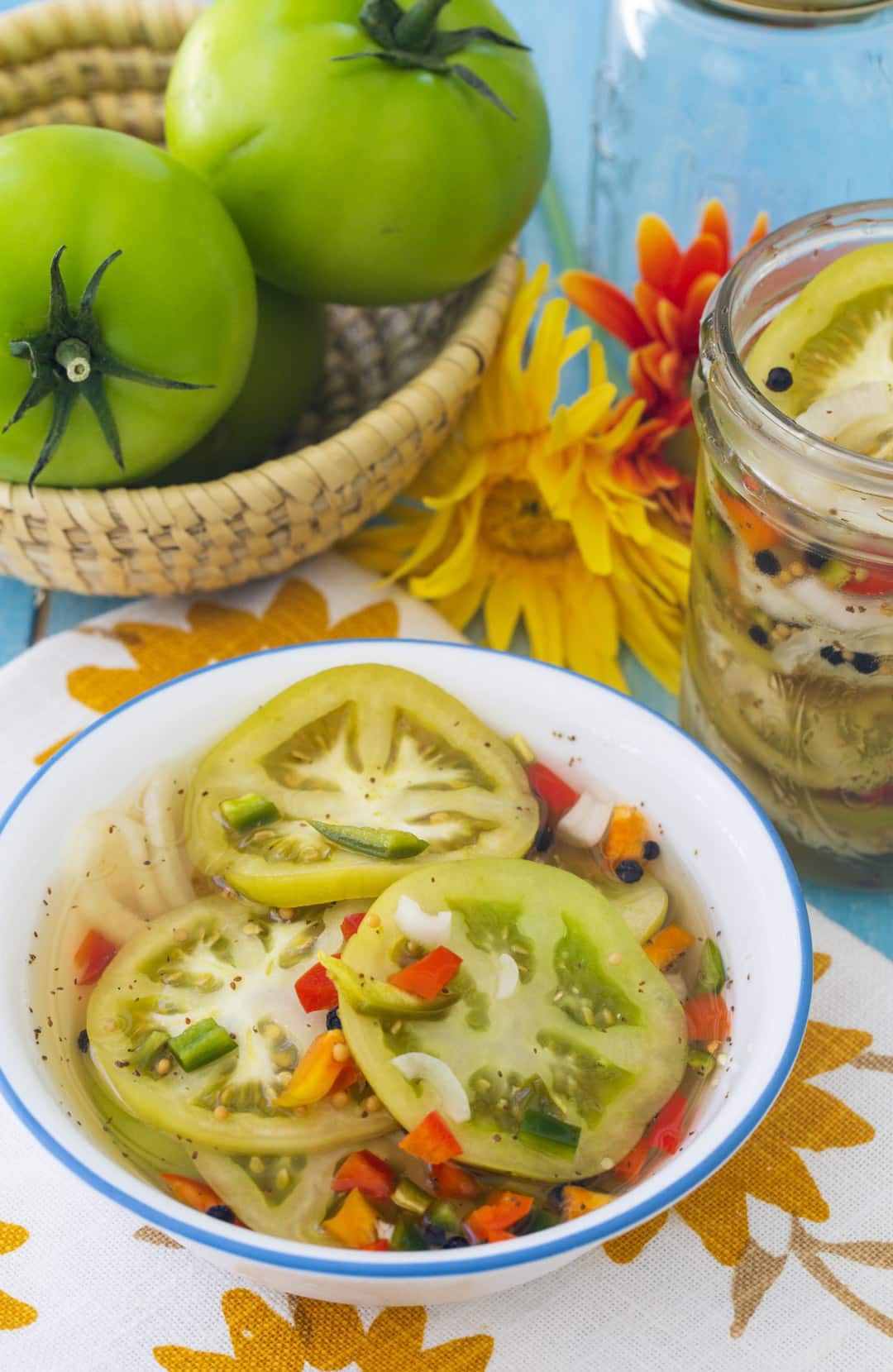 Pickled Green Tomatoes in a bowl with whole green tomatoes in background.