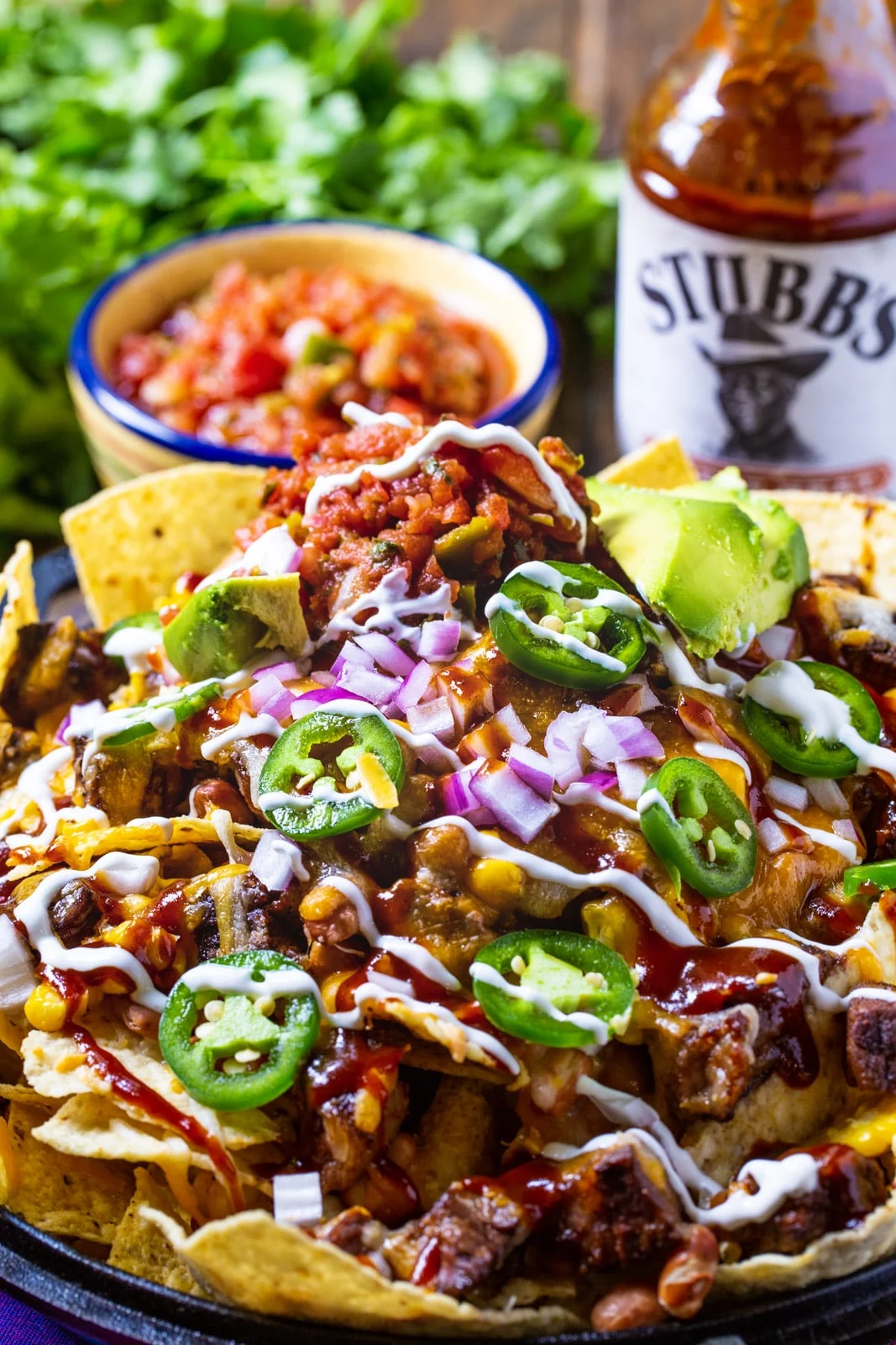 BBQ Steak Nachos in cast iron pan with cilantro and bowl of pico de gallo.