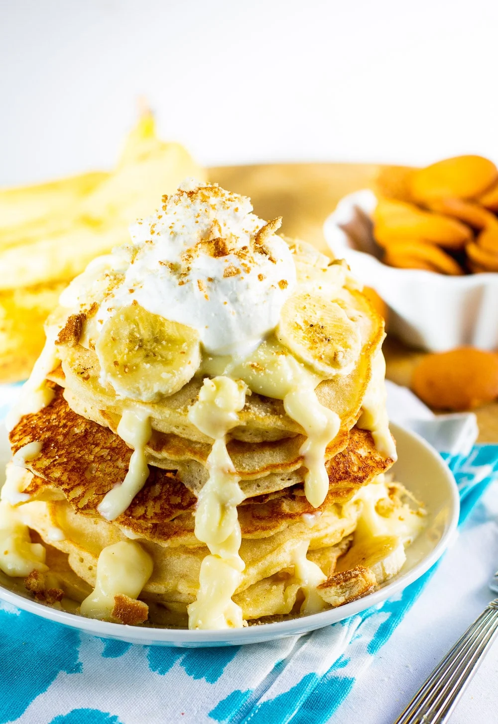 Pancakes on a plate with bananas and vanilla wafers in background.