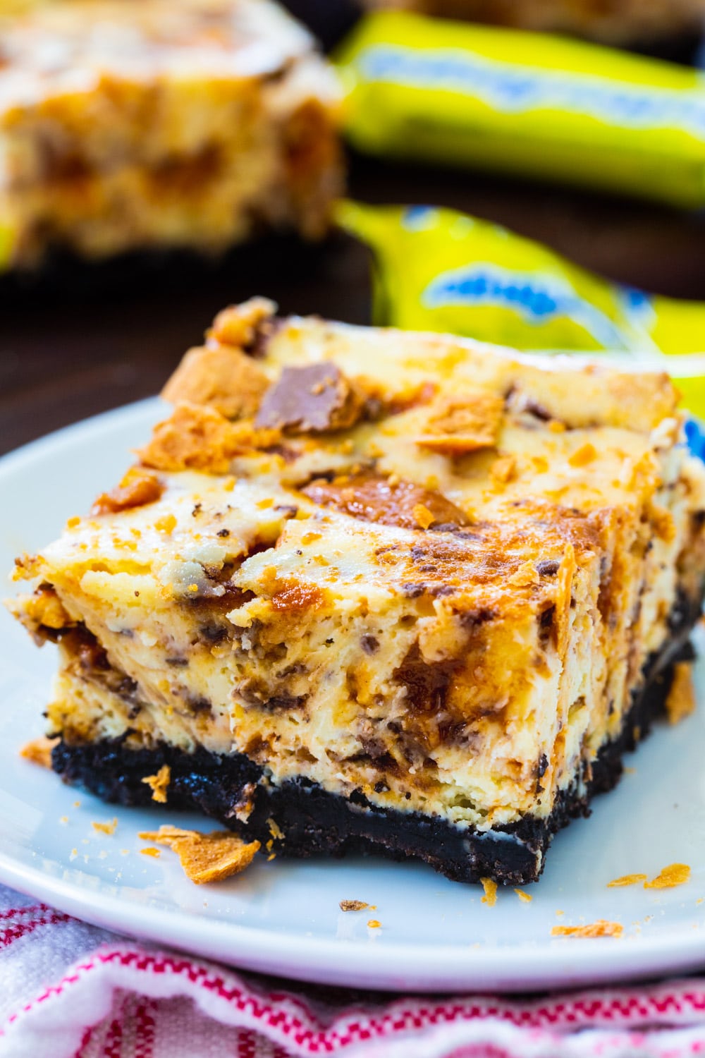 Butterfinger Cheesecake Bar on a small plate surrounded by mini butterfinger candies.