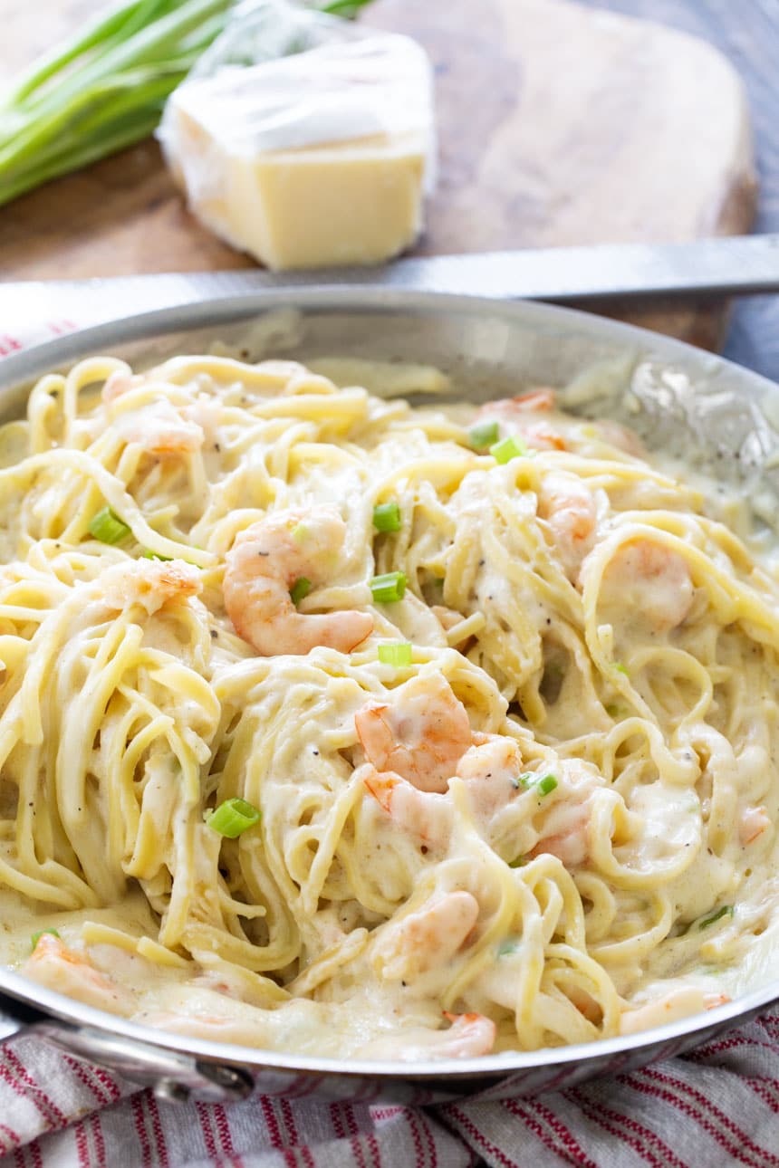 Pan full of Shrimp Alfredo with Parmesan cheese in background