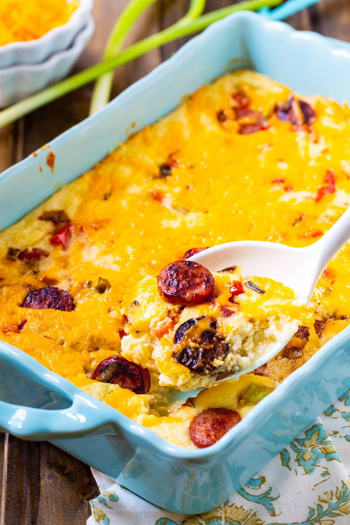 Spoon scooping up Cheesy Grits Casserole with Smoked Sausage.