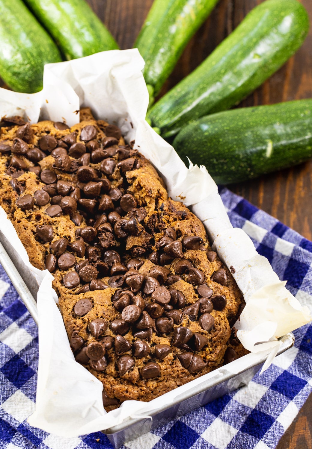 Zucchini Bread in loaf pan surrounded by fresh zucchini.