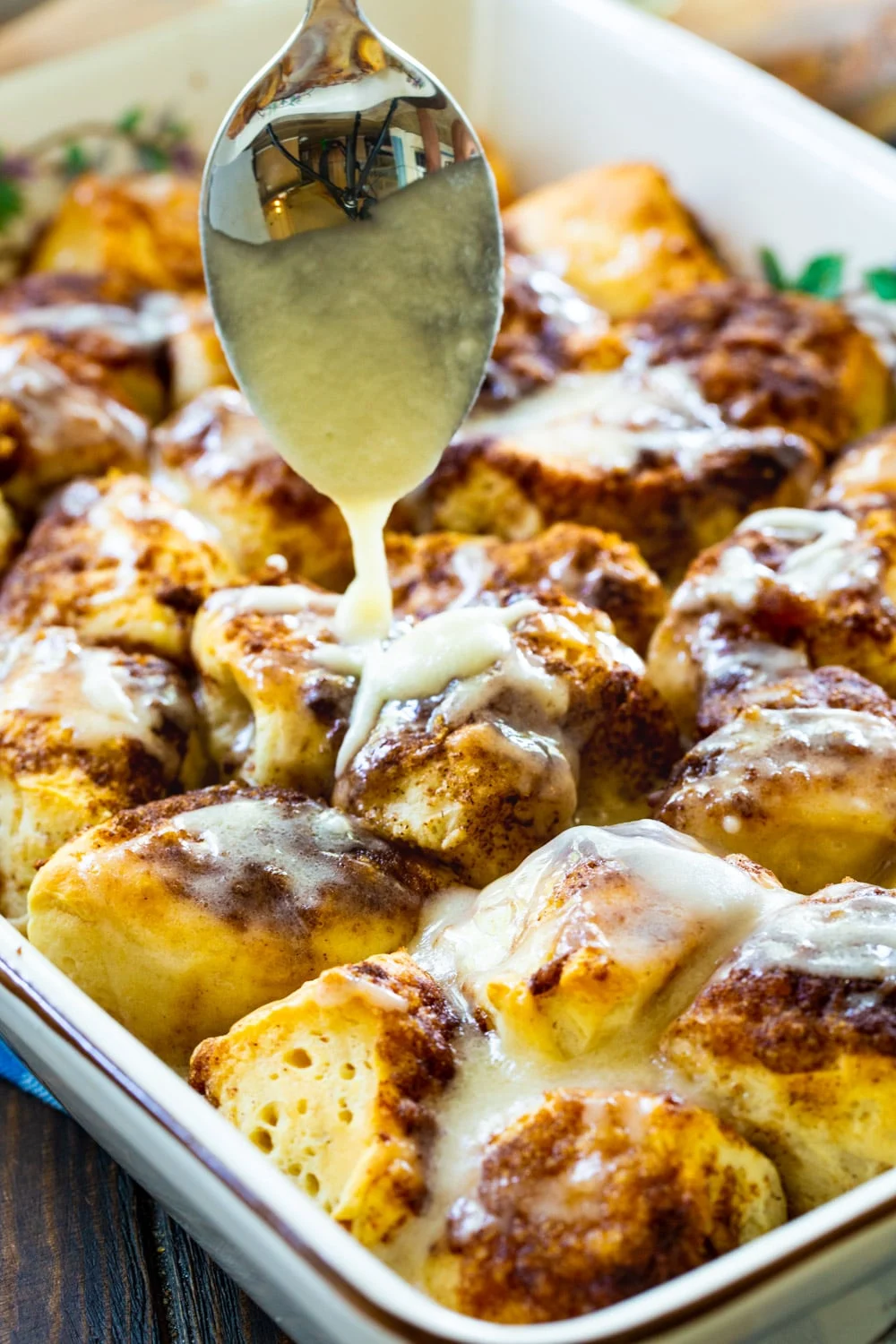 Spoon drizzling icing over cinnamon roll pieces.