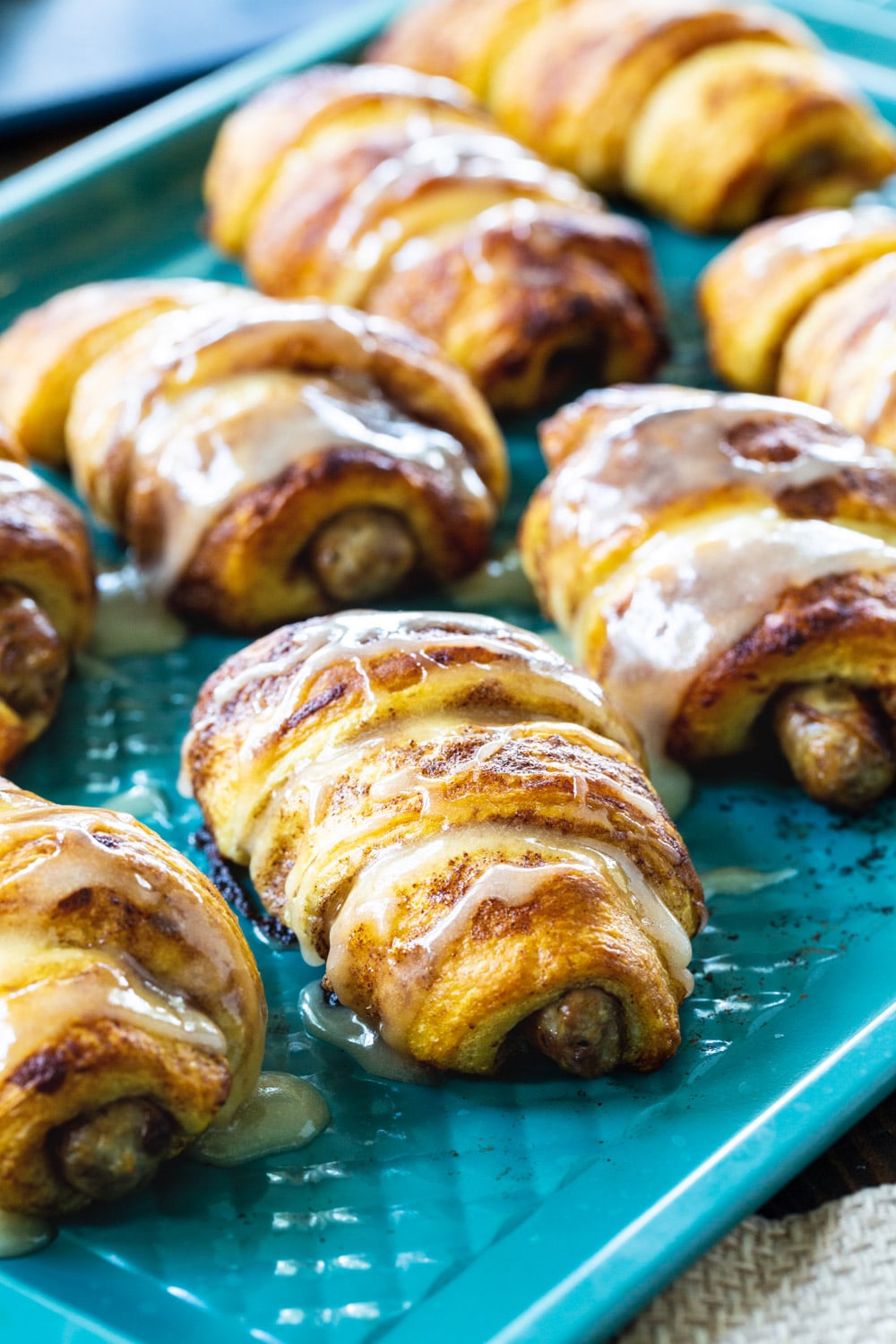 Cinnamon Roll Pigs in a Blanket on a blue baking sheet.