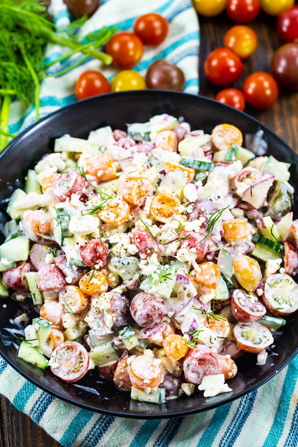 Salad in a black bowl with fresh tomatoes surrounding it.