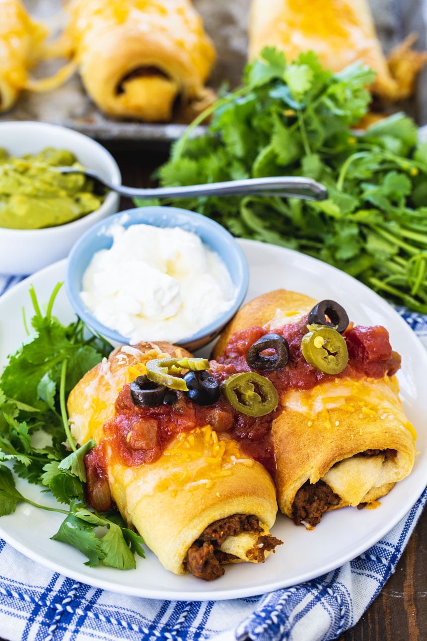 Two Beef Burritos on a plate with cilantro and more burritos in background.