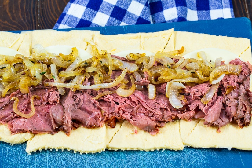 Roast beef and onions spread out on crescent roll dough.