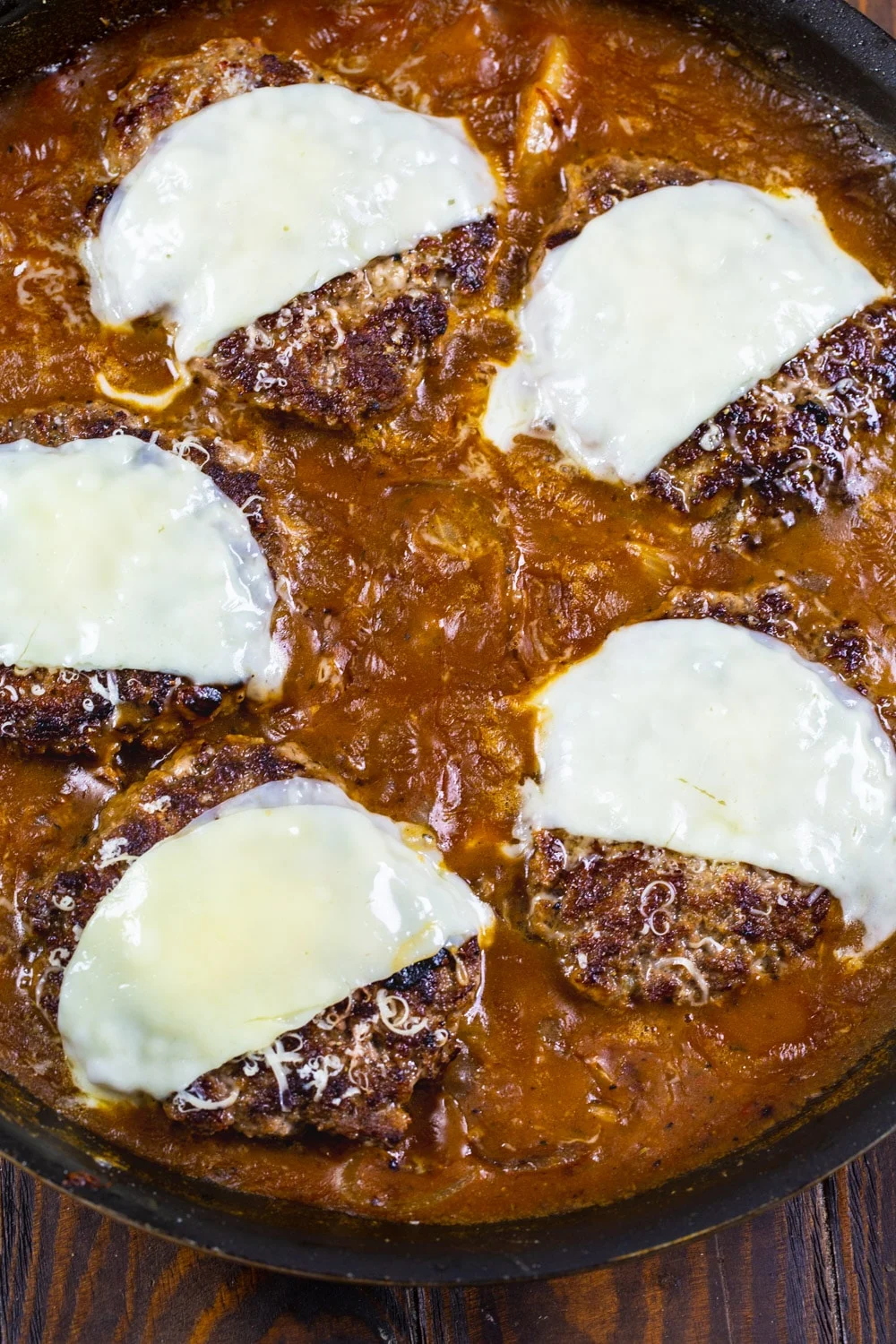 Salisbury Steak patties cobered with cheese in a skillet.