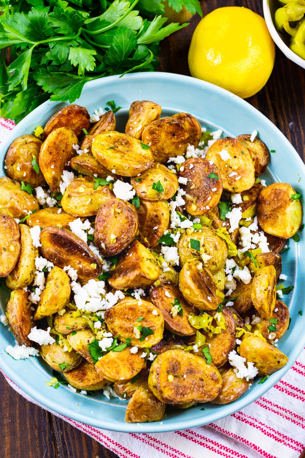 Greek Potatoes in a bowl surrounded by parsley and lemons.