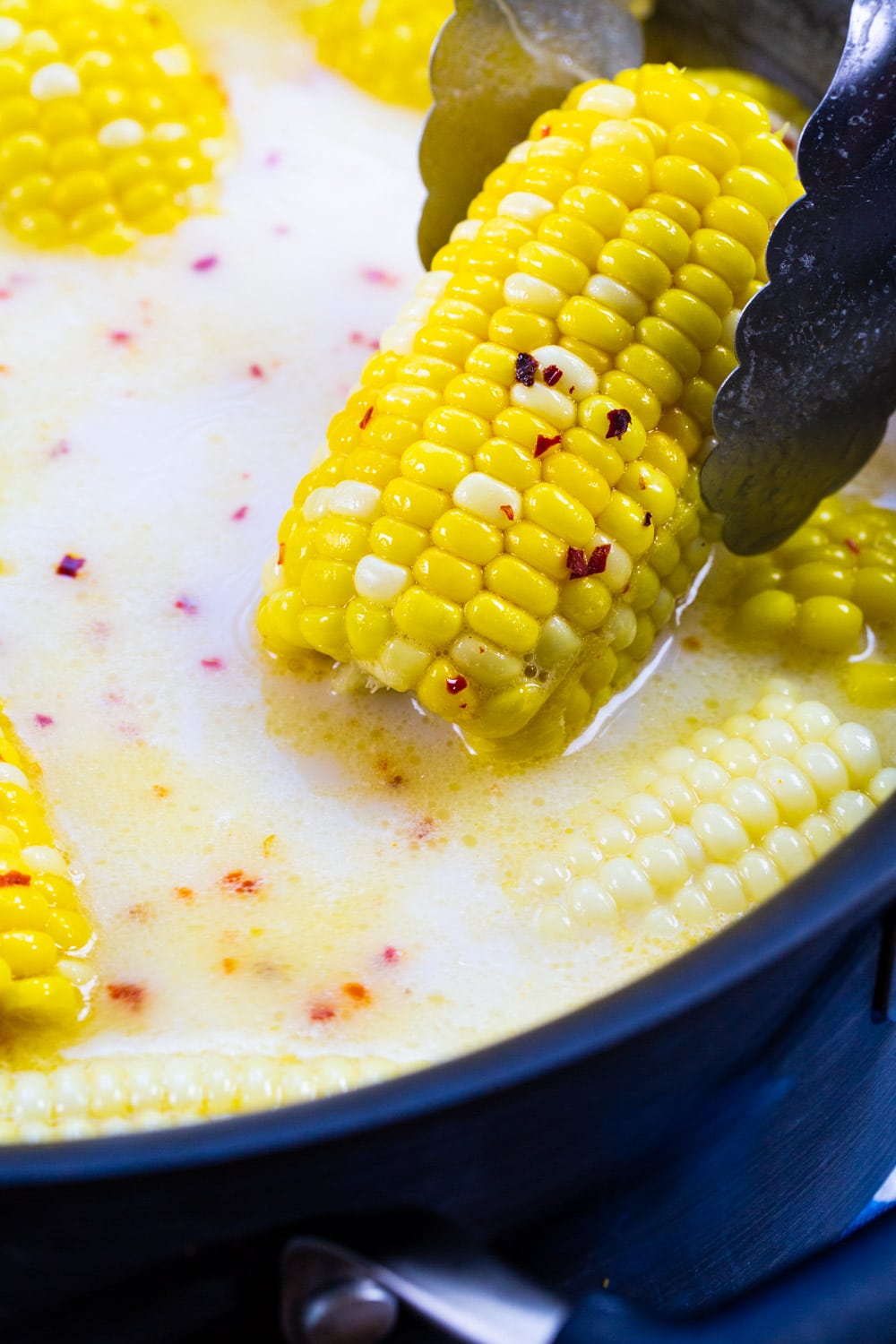 Tongs lifting piece of corn out of liquid.