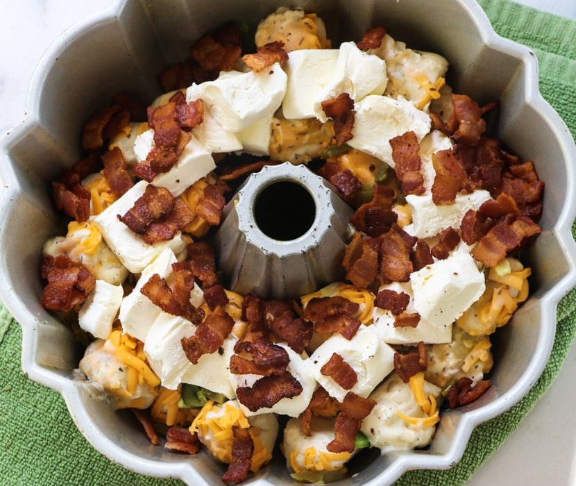 Cream cheese pieces and bacon placed on top of biscuit pieces.