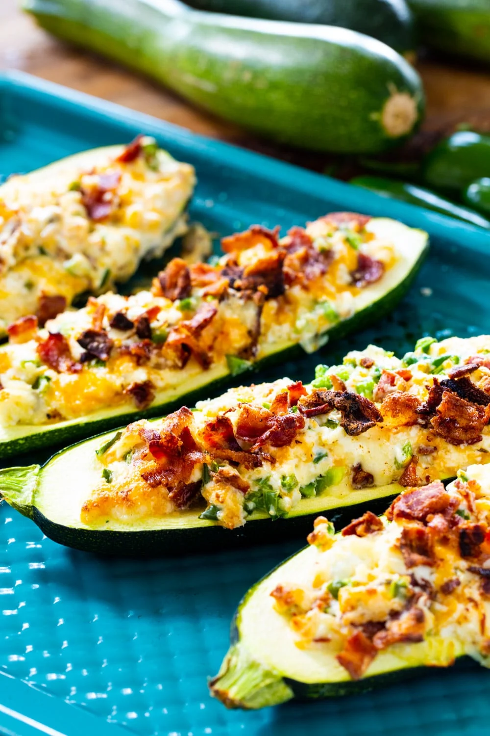 Jalapeno Popper Zucchini Boats on baking sheet with fresh zucchini in background.