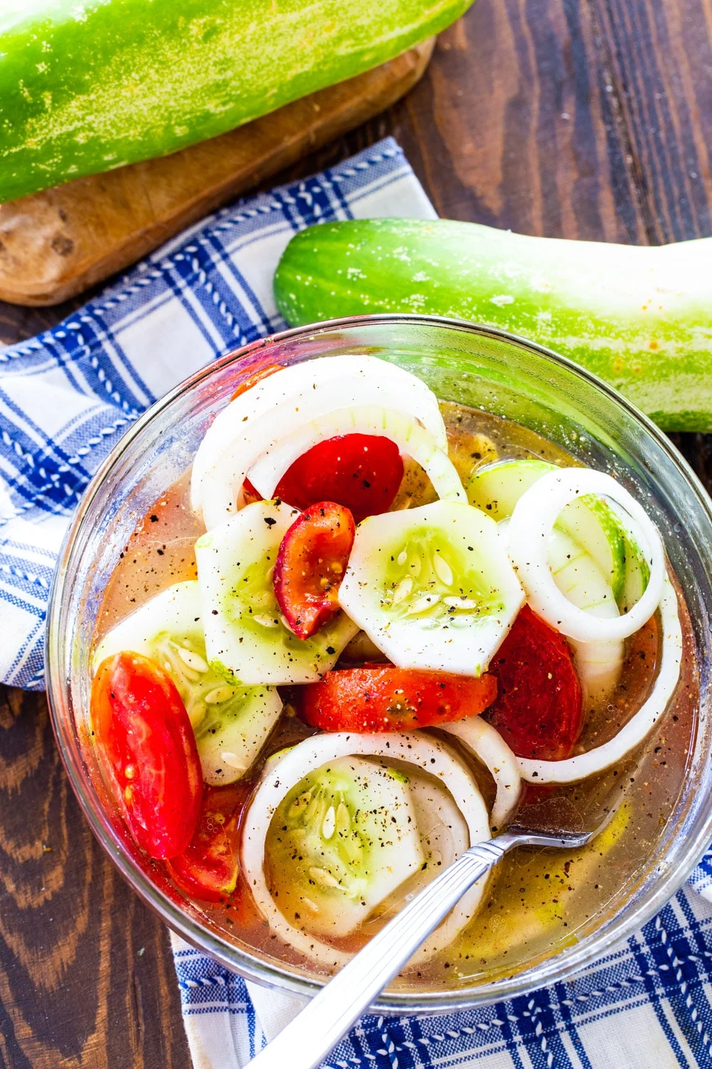 Cucumber Salad in glass bowl with whole cucumbers next to it.
