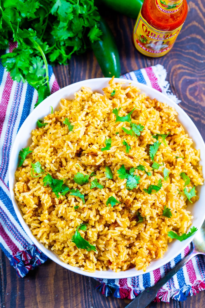 Overhead of Rice in a bowl with a bottle of hot sauce and bunch of cilantro.