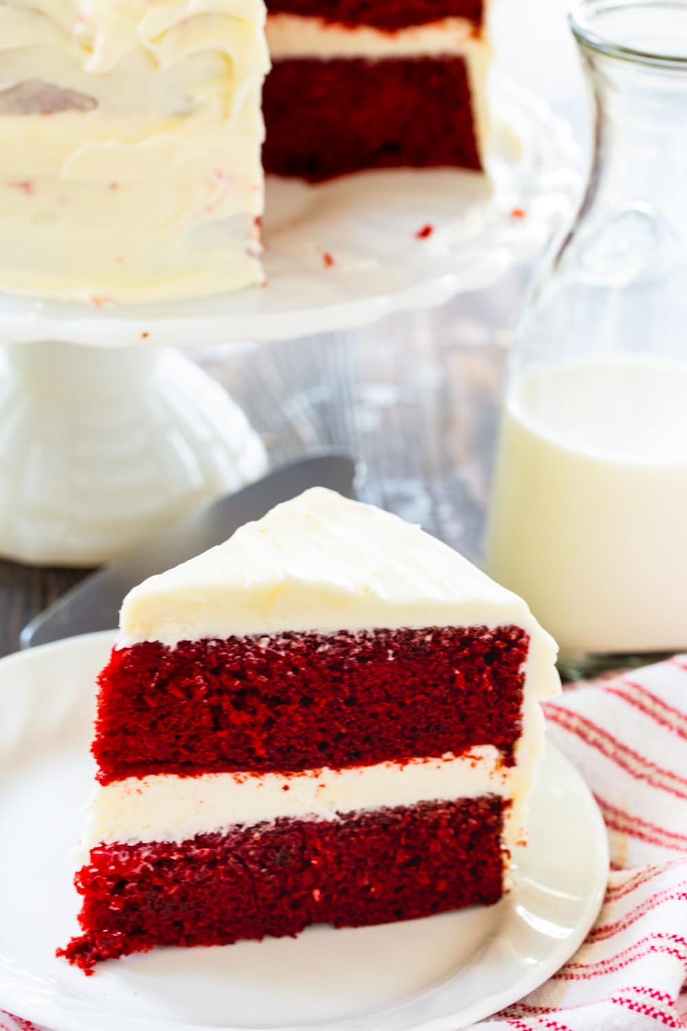 Slice of cake on plate with rest of cake on cake stand in background.