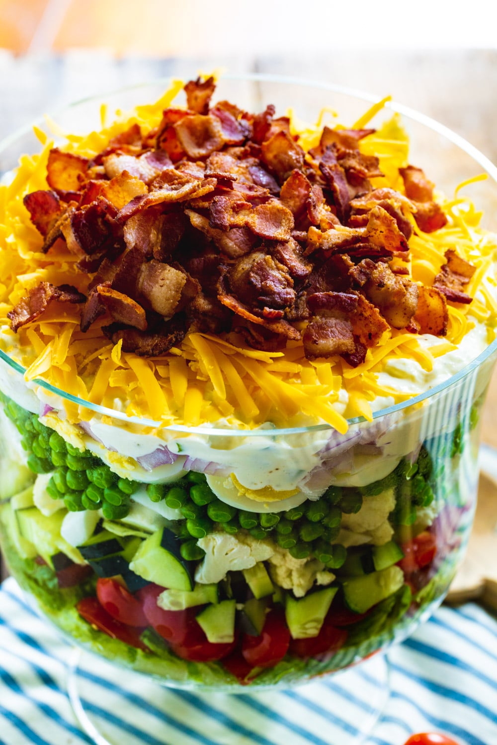 Layered Salad topped with cheese and bacon in a trifle dish.